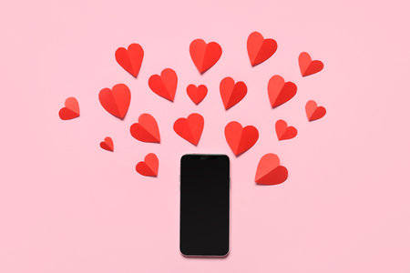 Composition with modern mobile phone and red paper hearts on pink background. Valentines Day celebrationの写真素材