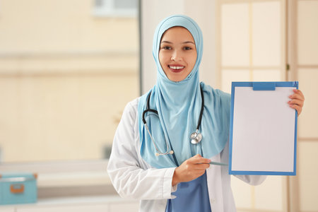 Female Muslim doctor in hijab with clipboard at clinic. World Hijab Day conceptの写真素材