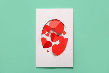 Composition with card and red paper hearts on color background. Valentines Day celebration