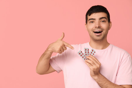 Young man pointing at blisters of vitamin A pills on pink backgroundの写真素材