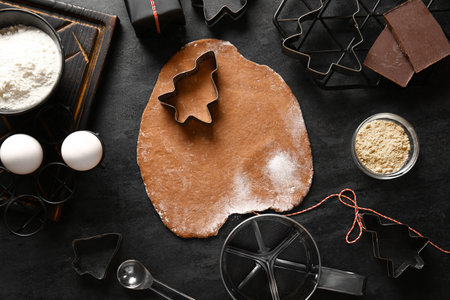Cutters, fresh dough and ingredients for gingerbread cookies on black backgroundの写真素材