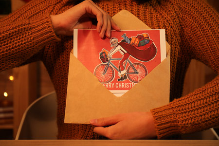 Woman holding envelope with Christmas greeting card at table in festive room, closeupの写真素材