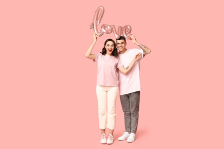 Loving young couple with balloon in the shape of the word LOVE on pink background. Celebration of Saint Valentine's Dayの写真素材