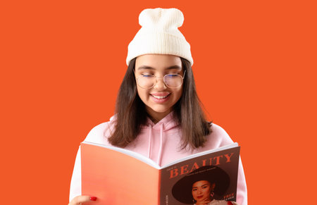 Young woman in eyeglasses reading magazine on orange background, closeupの写真素材