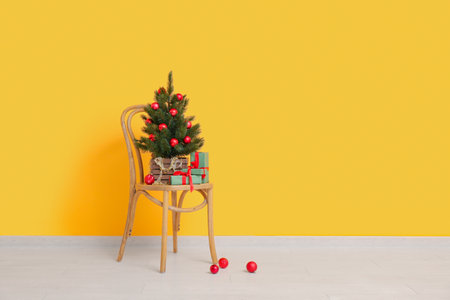 Wooden chair with Christmas tree in pot and gifts near orange wallの写真素材