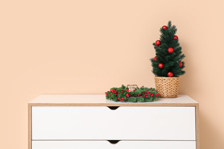 Dresser with Christmas tree in pot and wreath near beige wallの写真素材