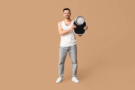 Handsome sporty young man with scales on brown background. Weight loss conceptの写真素材