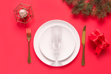 Beautiful table setting with Christmas tree branches, gift box and candle on red backgroundの写真素材