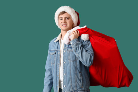 Happy young man in Santa hat with bag of gifts on green backgroundの写真素材