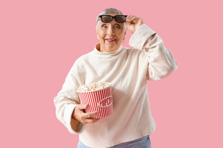 Senior woman with 3D glasses and popcorn on pink background