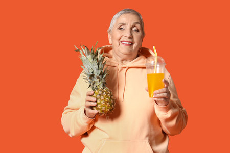 Senior woman with juice and pineapple on orange backgroundの写真素材