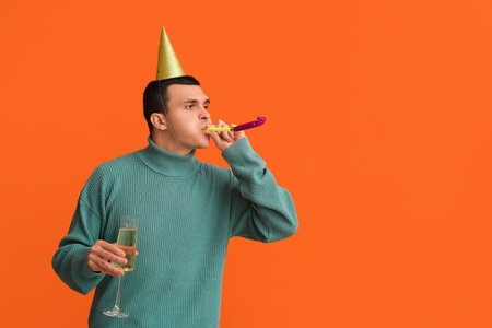 Young man in party hat with glass of champagne celebrating Christmas on orange backgroundの写真素材