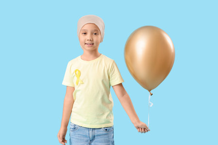 Little Asian girl after chemotherapy with ribbon and balloon on blue background. Childhood cancer awareness conceptの写真素材
