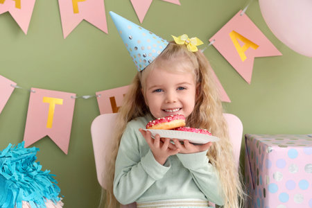 Cute little girl in party hat with donuts celebrating Birthday at home