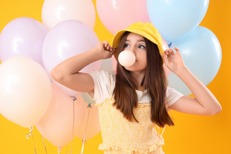 Trendy girl with balloons blowing bubble gum on yellow backgroundの写真素材