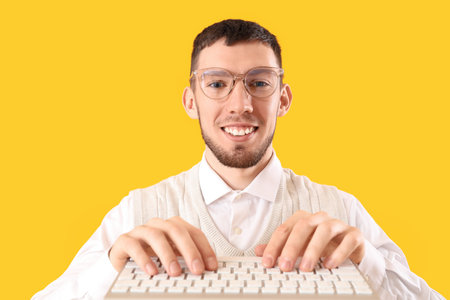 Young man in eyeglasses with computer keyboard on yellow background, closeupの写真素材