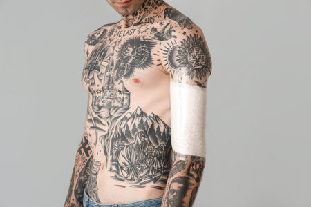 Tattooed man with protective film cover on his arm against gray background