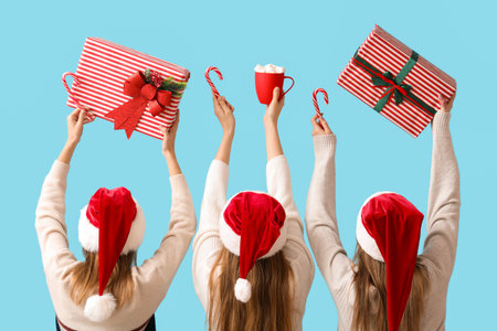 Women in Santa hats holding Christmas gifts on blue background, back viewの写真素材