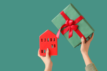 Hands holding Christmas gift and red house model on green backgroundの写真素材