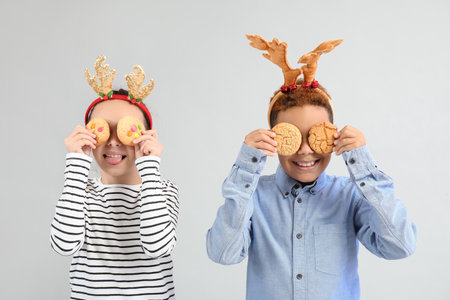 Funny little children in reindeer horns with cookies on gray backgroundの写真素材