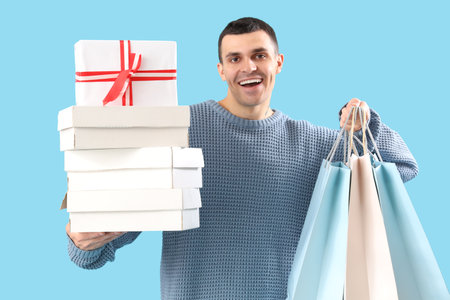 Handsome young happy man with gift boxes and shopping bags on blue backgroundの写真素材