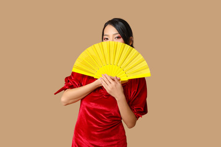 Beautiful young Asian woman with fan on brown background. Chinese New Year celebrationの写真素材