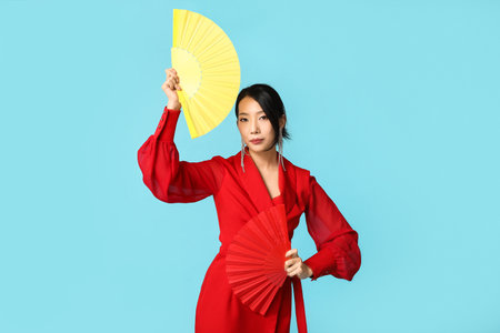 Beautiful young Asian woman with fans on blue background. Chinese New Year celebrationの写真素材
