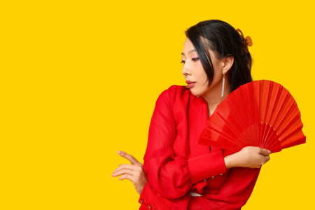 Beautiful young Asian woman with fan on yellow background. Chinese New Year celebrationの写真素材