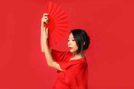 Beautiful young Asian woman with fan on red background. Chinese New Year celebrationの写真素材