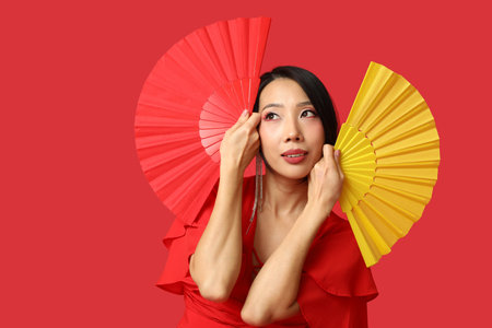 Beautiful young Asian woman with fans on red background. Chinese New Year celebrationの写真素材