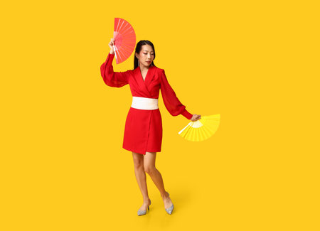 Beautiful young Asian woman with fans on yellow background. Chinese New Year celebrationの写真素材