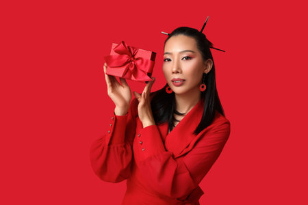 Beautiful young Asian woman with gift box on red background. Chinese New Year celebrationの写真素材