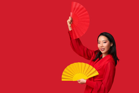 Beautiful young happy Asian woman with fans on red background. Chinese New Year celebration