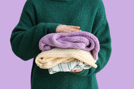 Woman holding stack of different stylish sweaters on purple backgroundの写真素材