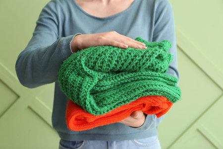 Woman holding stack of different stylish sweaters on green background