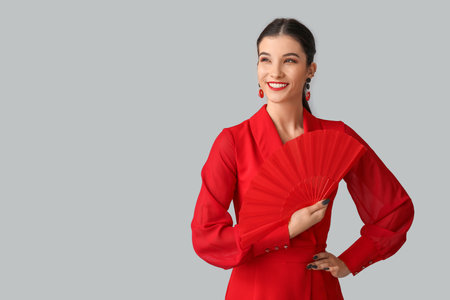Beautiful young happy woman with fan on gray background. Chinese New Year celebrationの写真素材