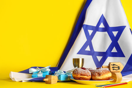 Israel flag with tasty donuts, gift boxes, dreidels and cup on yellow background. Hanukkah celebrationの写真素材