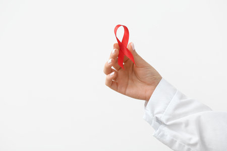Young female doctor with red ribbon on white background, closeup. AIDS Day conceptの写真素材