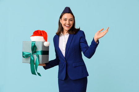 Beautiful stewardess with gift box and Santa hat on blue backgroundの写真素材
