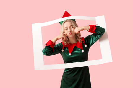 Funny young woman dressed as elf with frame on pink background