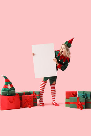 Shocked young woman dressed as elf with Christmas gifts and blank poster on pink backgroundの写真素材
