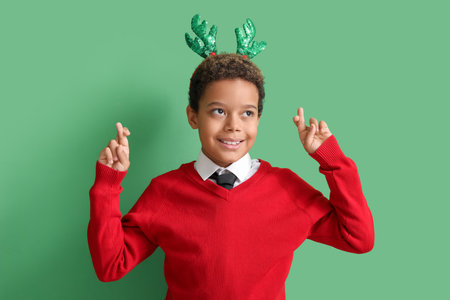 Little African-American boy in reindeer horns making wish on green backgroundの写真素材