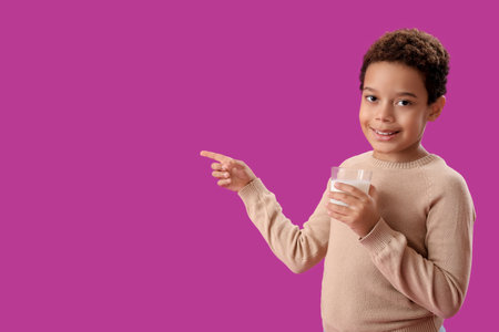 Little African-American boy with glass cup of milk pointing at something on purple backgroundの写真素材