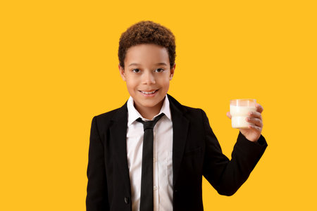 Little African-American boy with glass of milk on yellow backgroundの写真素材