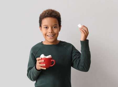 Little African-American boy holding cup of hot chocolate with marshmallows on white backgroundの写真素材
