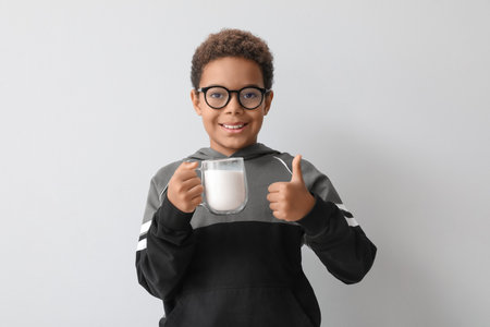 Little African-American boy with glass cup of milk showing thumb-up on white backgroundの写真素材