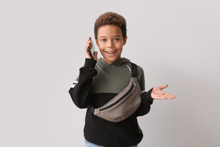 Little African-American boy talking by mobile phone on white background