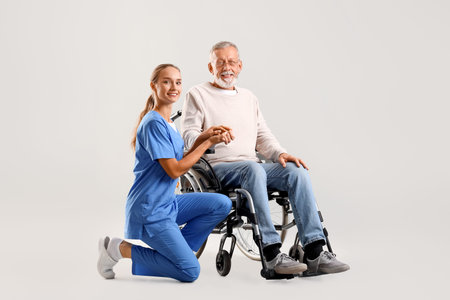 Senior man in wheelchair with nurse on light background