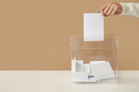 Hand putting paper voting in ballot box on beige backgroundの写真素材