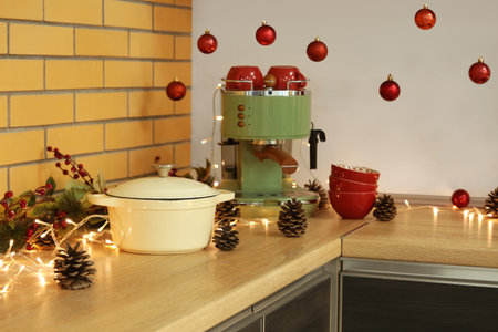 Coffee machine with fir cones and Christmas lights on counter in kitchen